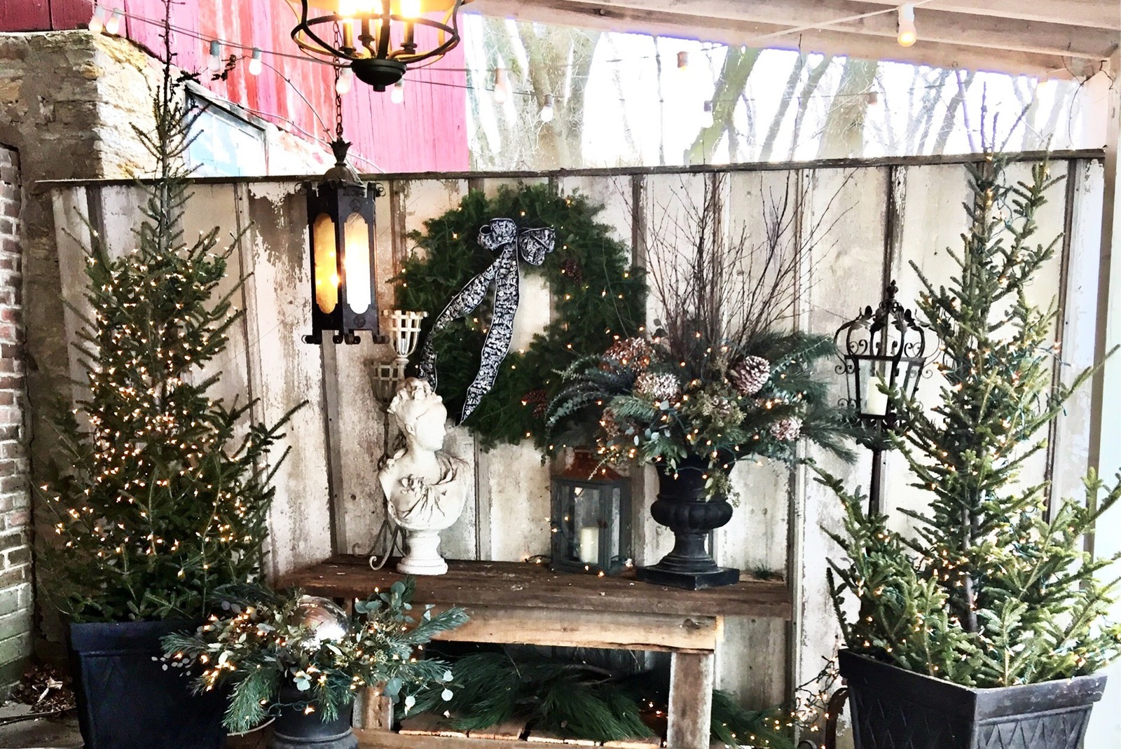 Rustic winter floral display featuring evergreen trees, a holiday wreath, lanterns, and seasonal greenery at Camrose Hill Flower Studio in Stillwater, Minnesota.