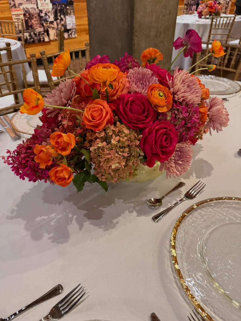 Colorful wedding centerpiece featuring vibrant orange roses, fuchsia blooms and pink flowers by Camrose Hill Flower Studio