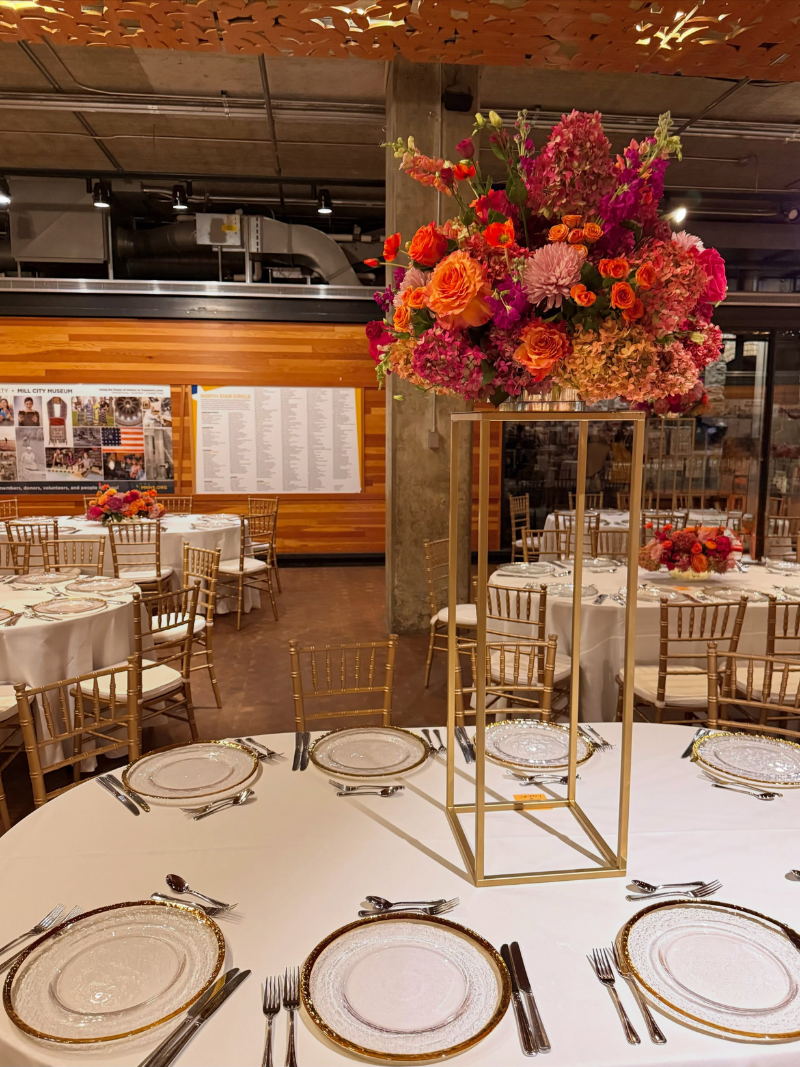 Tall gold centerpiece stand topped with vibrant pink and orange wedding flowers at an off-site reception