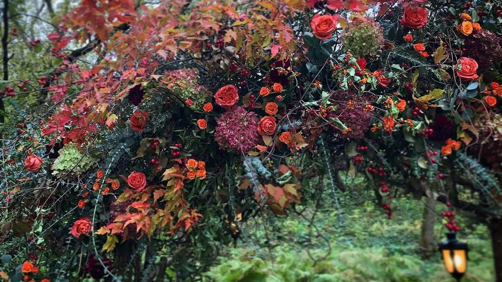 Autumn floral installation with orange roses, colorful foliage, and a hanging lantern at Camrose Hill